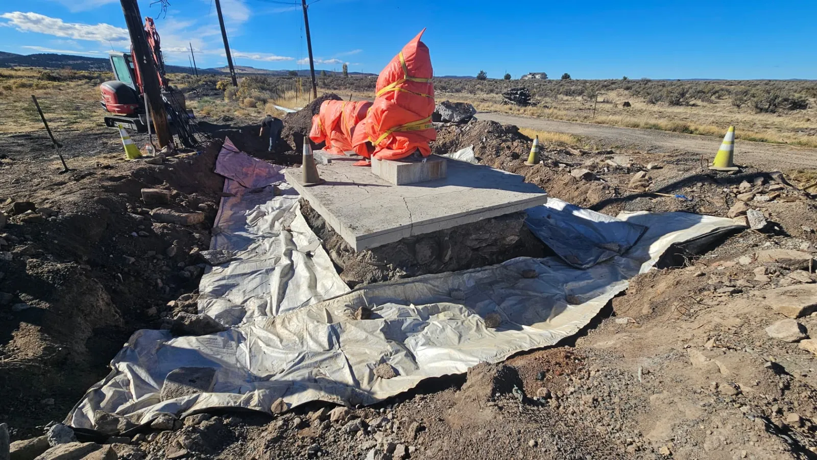 Excavation for new footings covered with insulated concrete blankets in Burns, Oregon, with an excavator on site