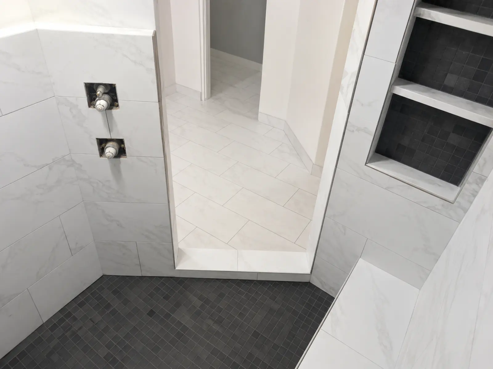 Large-format white marble shower with contrasting mosaic floor in progress by Almog Construction.