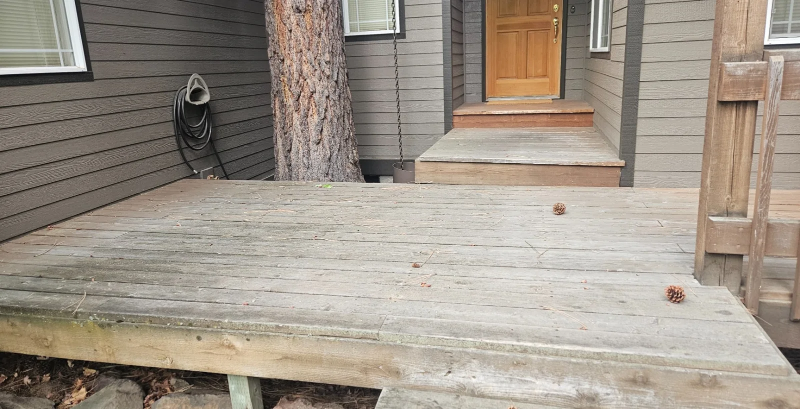 Weathered front deck and steps beside a tree and wood front door in Bend, Oregon