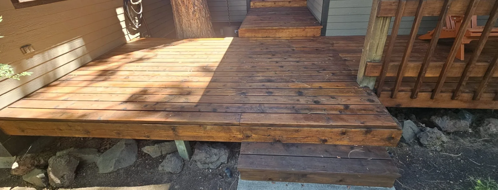 Stained front deck and steps beside a tree, wood railing and orange chairs in Bend, Oregon