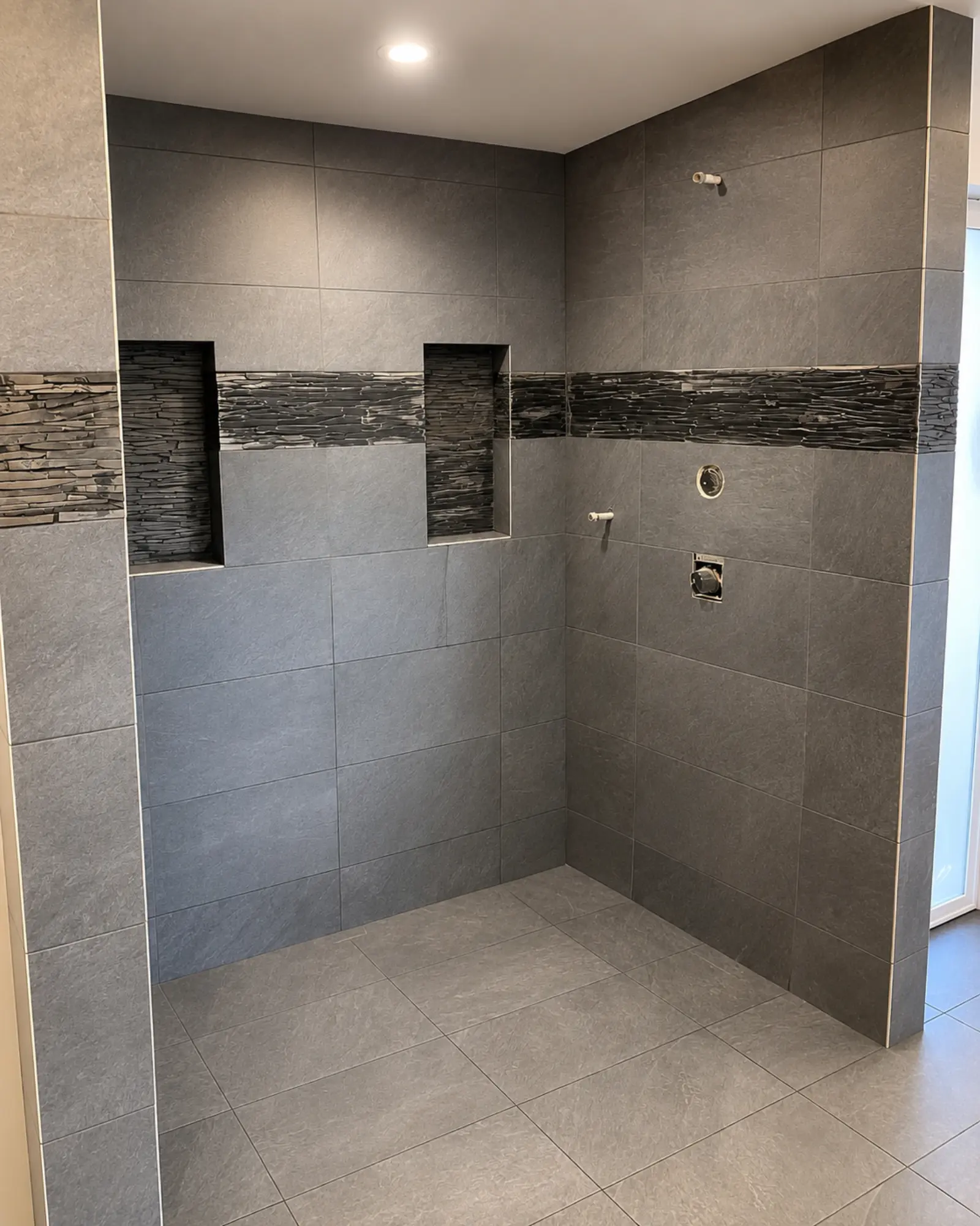 Modern shower under construction with gray tiles by Almog Construction.