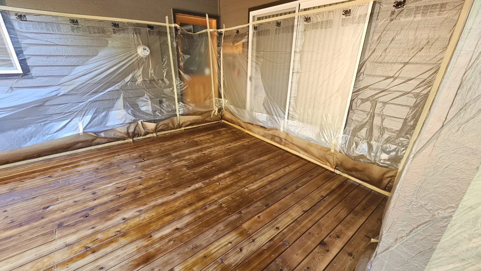 Stained deck boards beside windows and siding masked with plastic sheeting in Bend, Oregon